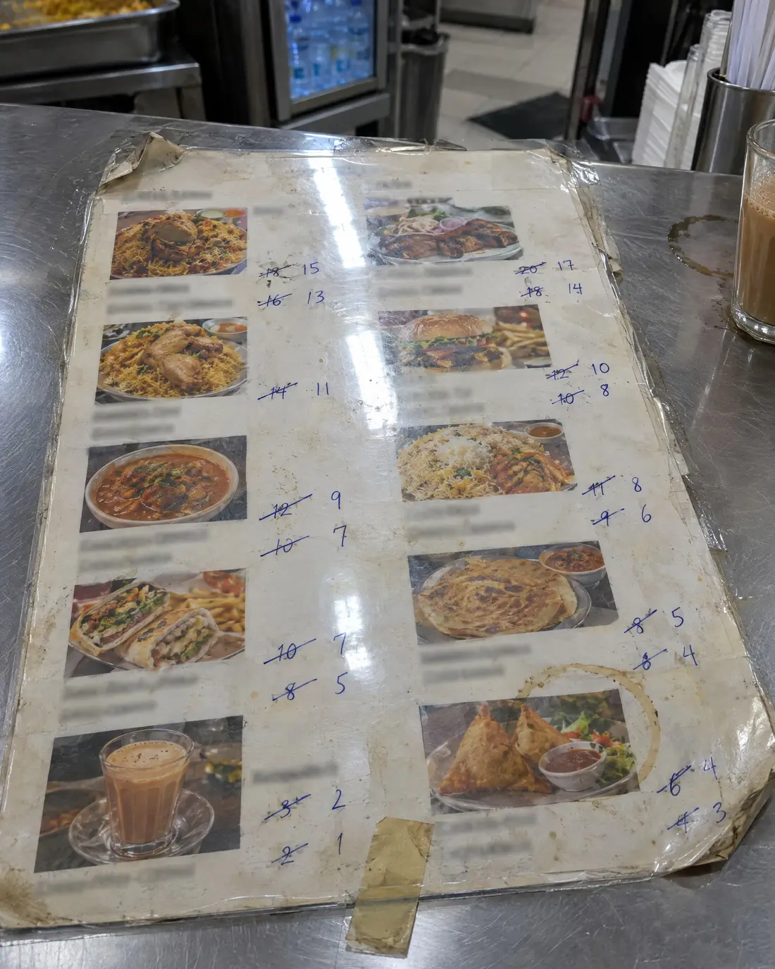 A laminated menu taped to a counter, old prices crossed out by hand